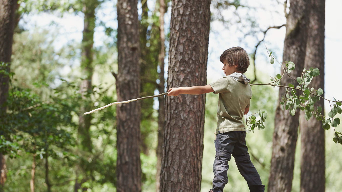 boy in the forest holding a very long branch like a javelin