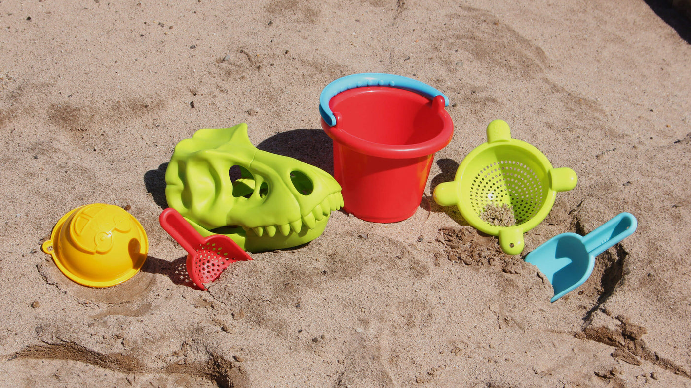 HABA sand toys set including bucket, sieve, mold, and scoops, and dino scoop sand glove in the sand