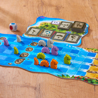 Water Dragons game board with gray, purple, green, and orange wooden pieces, cardboard game board, wooden die, and cards on a wooden table