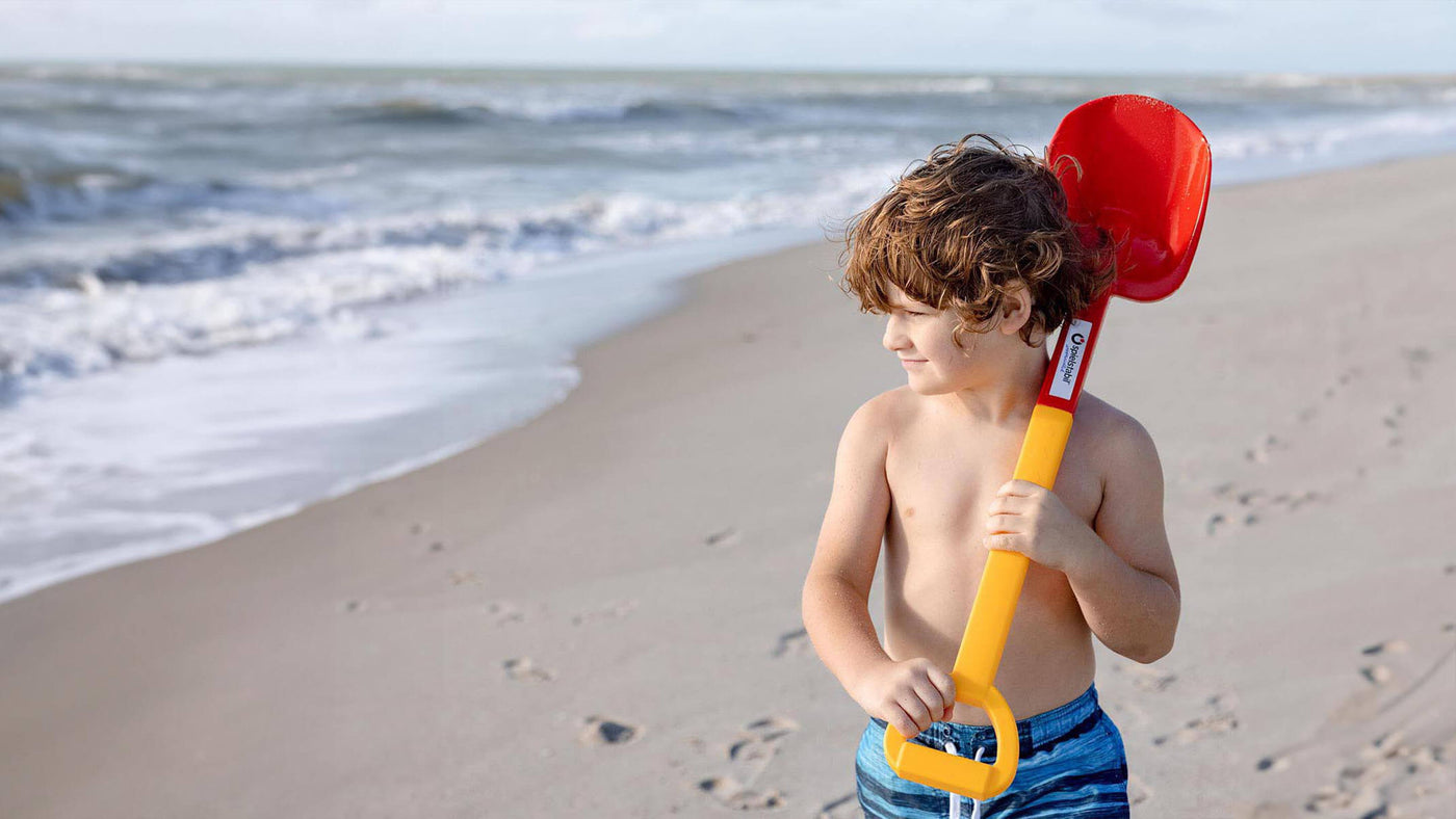 Boy at beach looking out at the ocean with a Spielstabil Long Handled Heavy Duty Beach Shovel over his shoulder