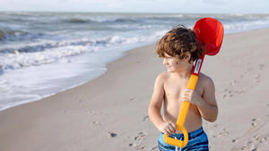 Boy at beach looking out at the ocean with a Spielstabil Long Handled Heavy Duty Beach Shovel over his shoulder