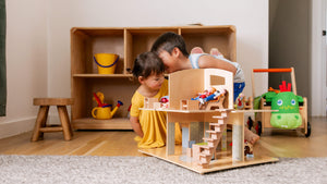 Two kids in a playroom whispering to each other while playing with Little Friends Dollhouse