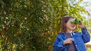 Girl outside in a dense leafy area looking through HABA Terra Kids Binoculars