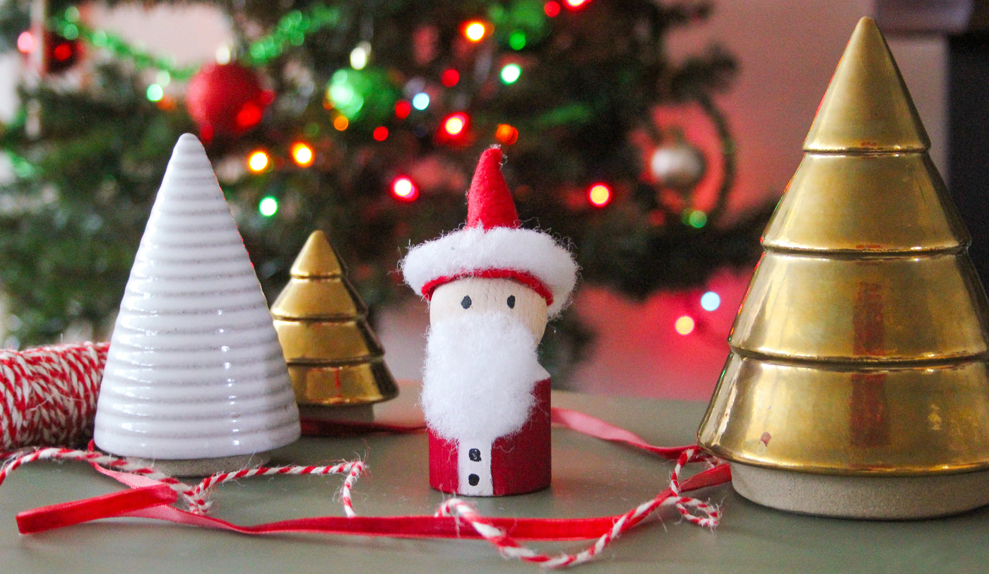 A DIY HABA Block Santa sits with ceramic trees and Christmas tree lights.