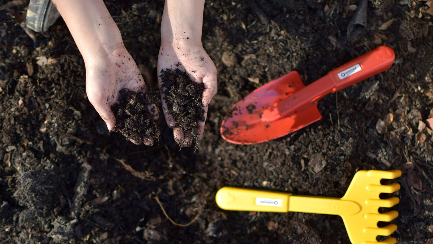 Child's hands holding soil with Spielstabil gardening tools in the background