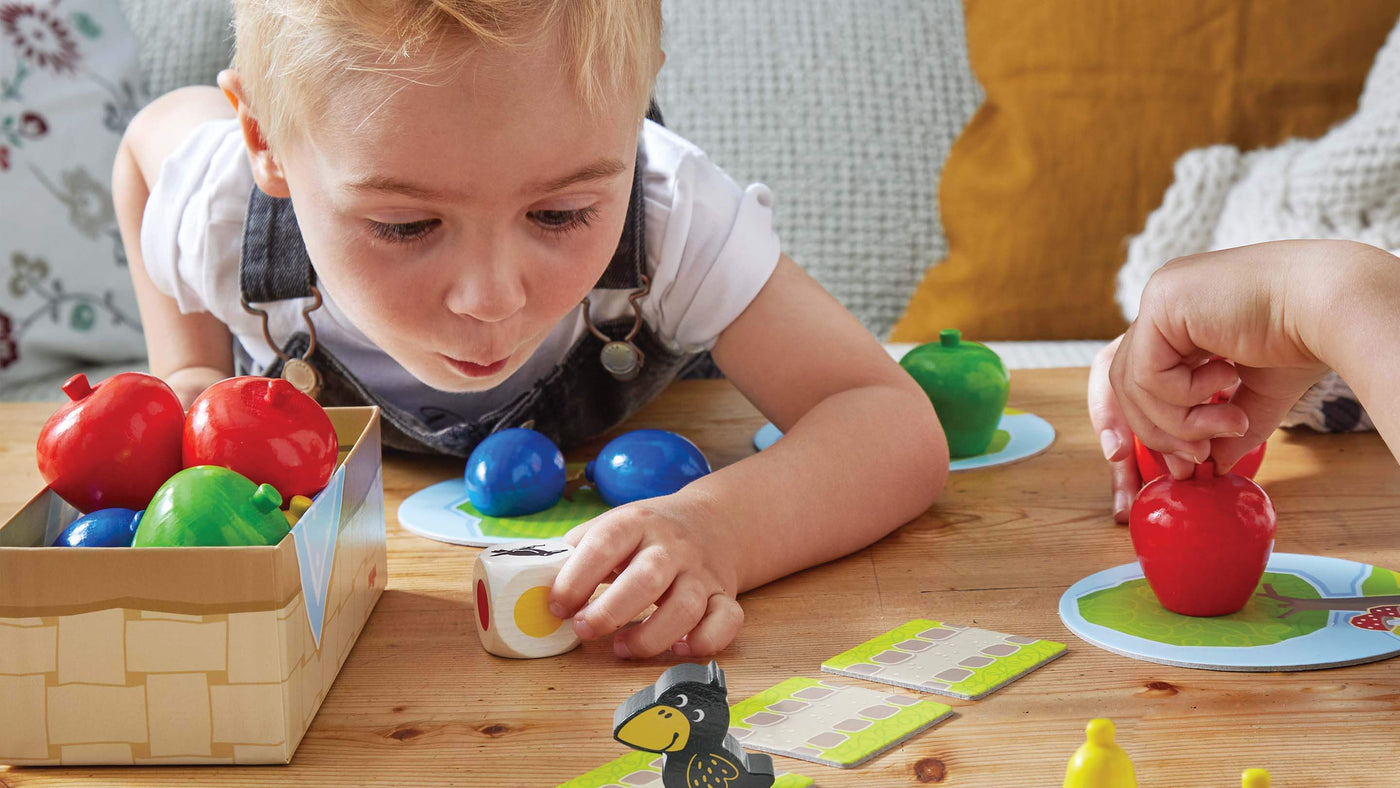 Boy leaning down to pick up a die from HABA's First Orchard game