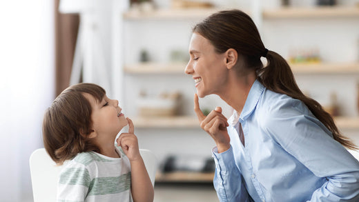 A woman and a young boy smiling at each other, both pointing to their chins.