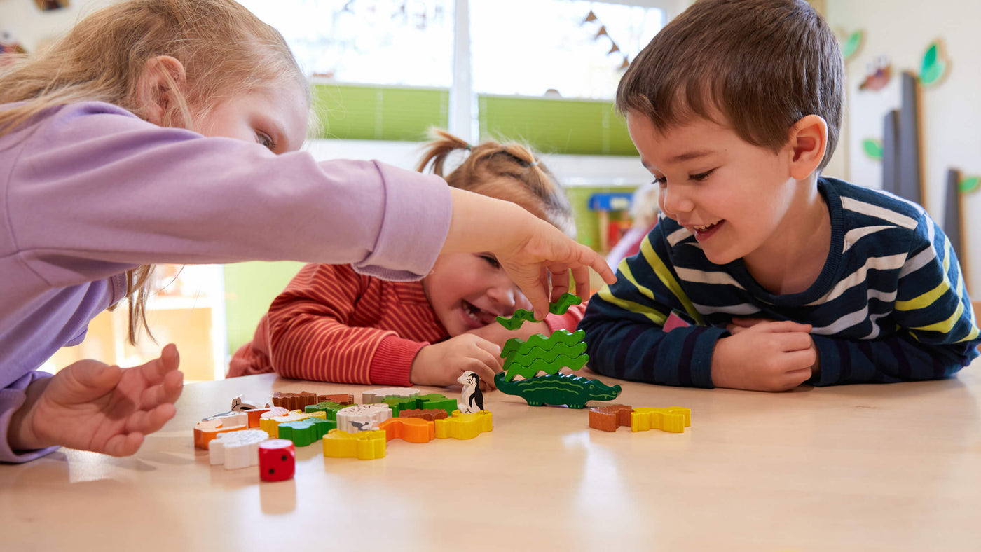 Three children in a classroom on a sunny day stacking wooden animal shapes