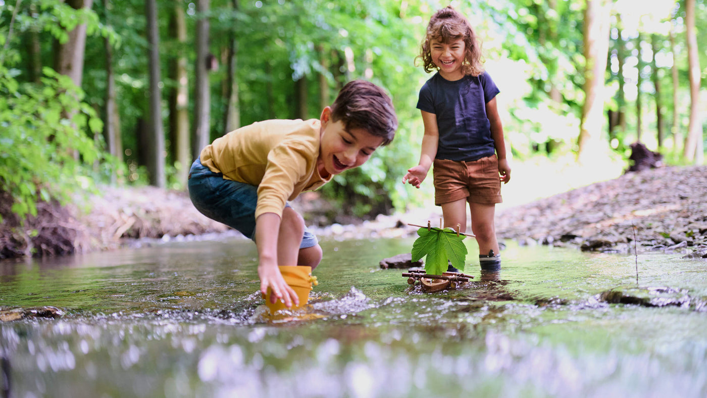 Boy and Girl outside in the day playing with Terra Kids Cork Boat in a creek