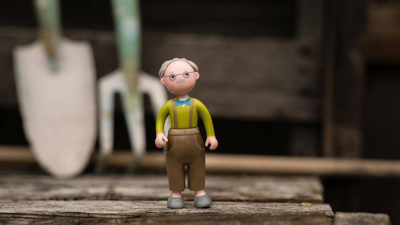 Toy farmer standing on a wood table with a pitchfork and shovel in the background