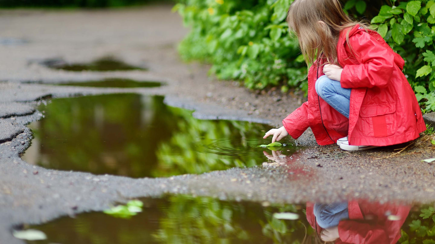 A girl playing in a puddle on rainy summer day