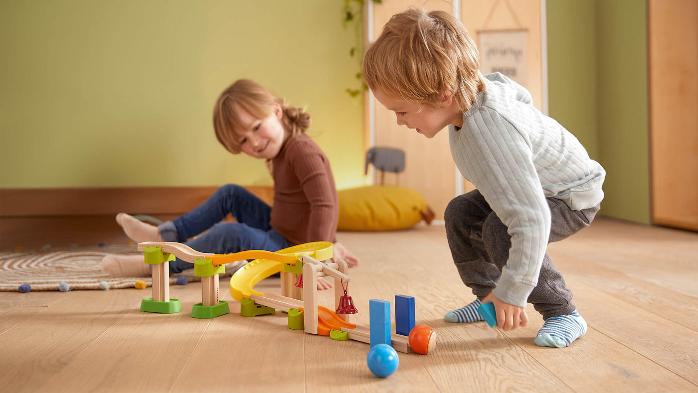 Two children playing with a Kullerbu toy track set on a wooden floor.