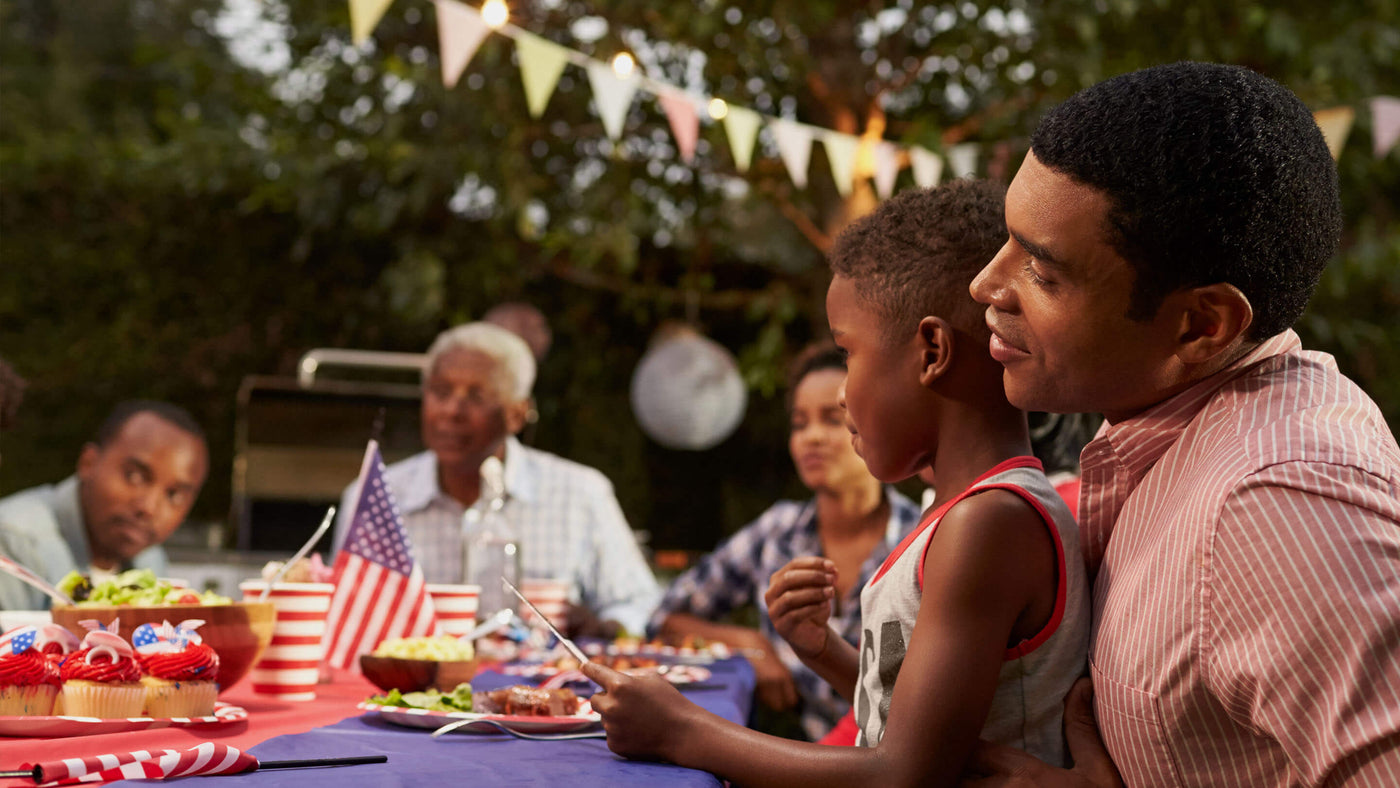 Family sitting around an outdoor table with food celebrating the fourth of July