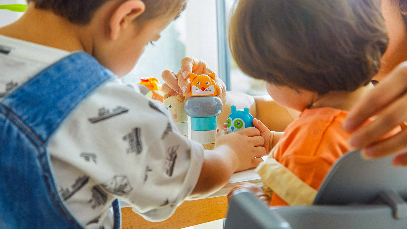 Two young children playing with colorful wooden animal-shaped toys at a table.