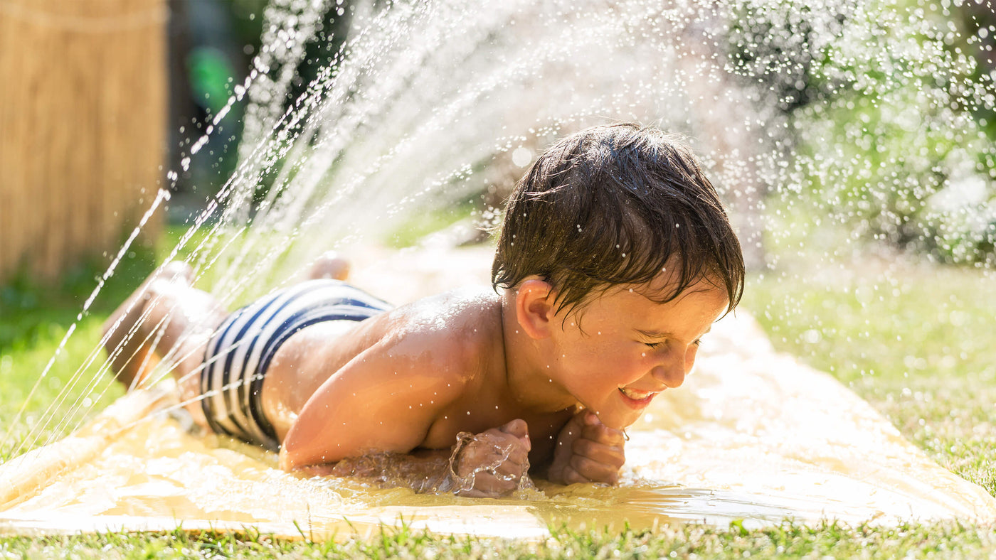 Boy outside in summer playing on a water slip and slide