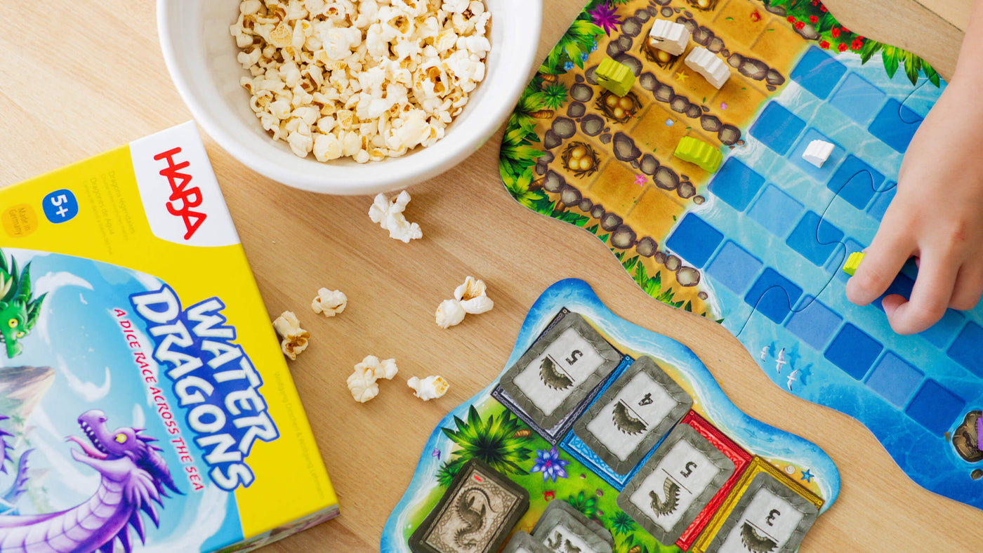 Overhead view of a hand reaching for a game piece of the HABA game Water Dragons with popcorn