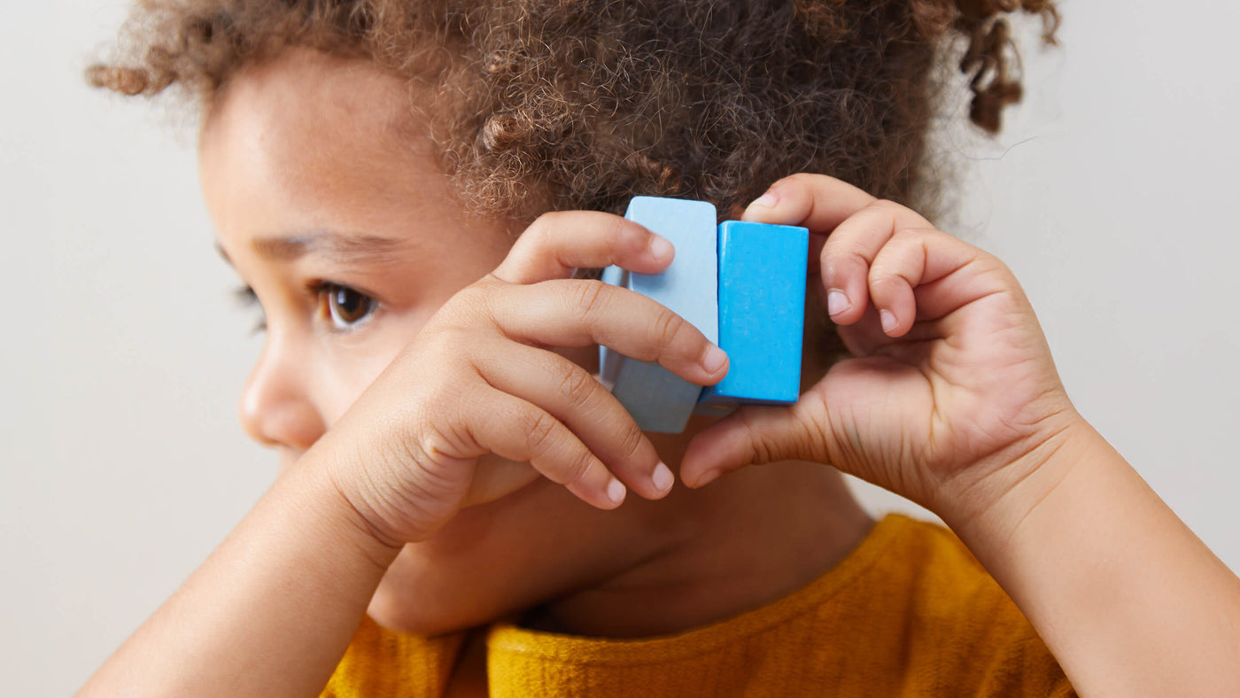 A child holding a 2-tone blue wooden block near their face.