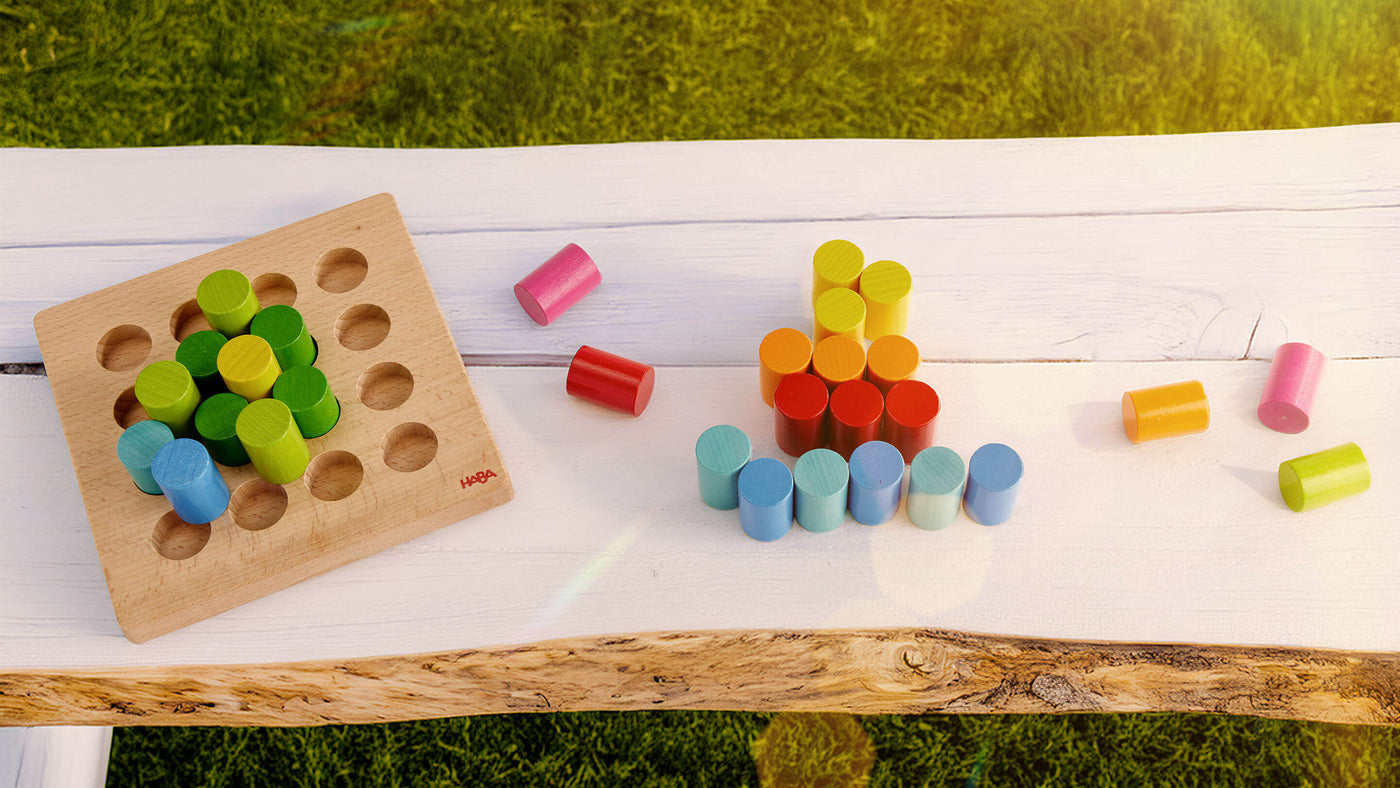 Colorful wooden cylinders on a white bench with a grassy background.