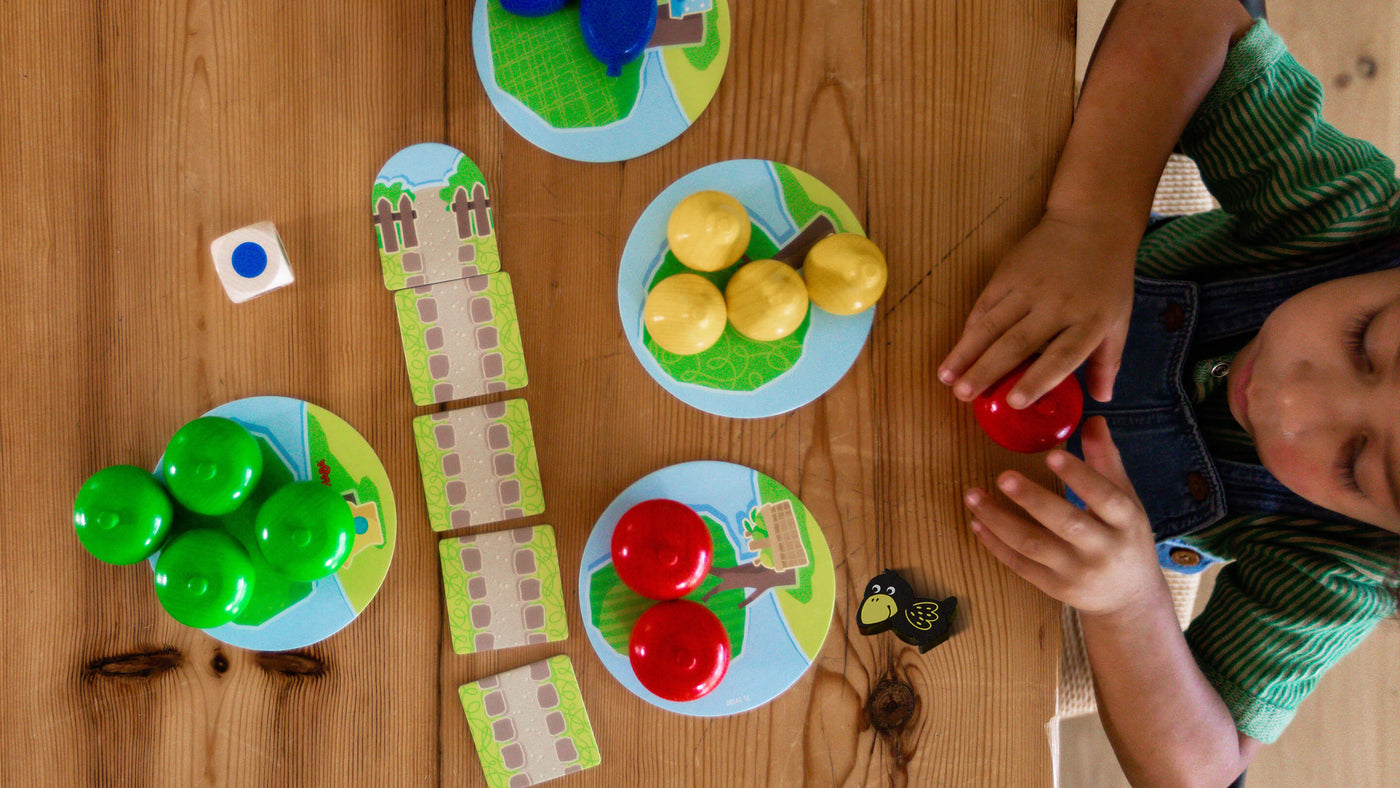 Child playing HABA First Orchard board game with colorful pieces on a wooden table.