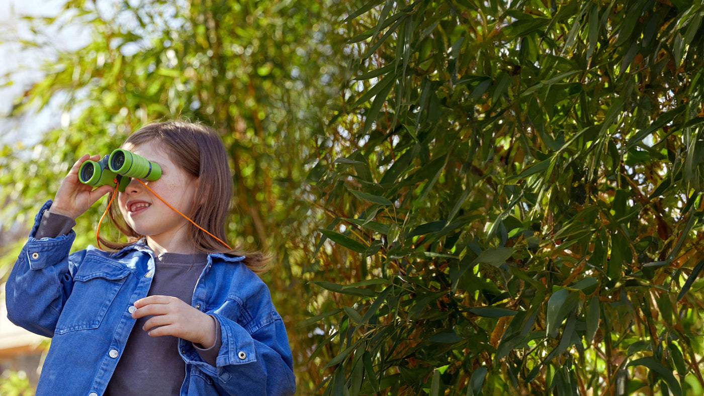 Girl outside in a dense leafy area looking through HABA Terra Kids Binoculars