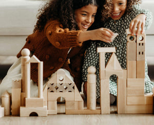 Two girls sitting on the floor building a castle out of HABA wooden blocks