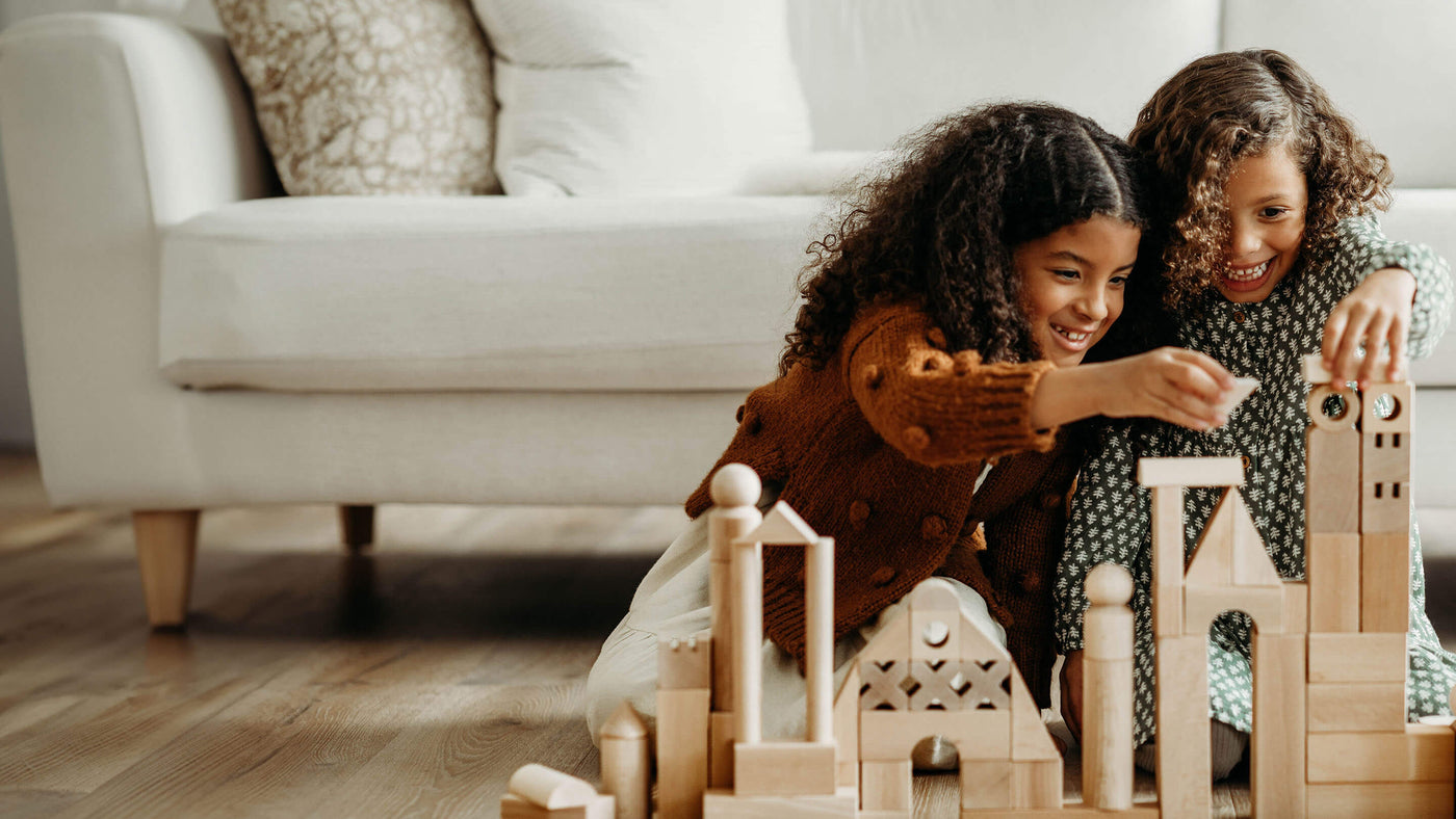 Two girls sitting on the floor building a castle out of HABA wooden blocks
