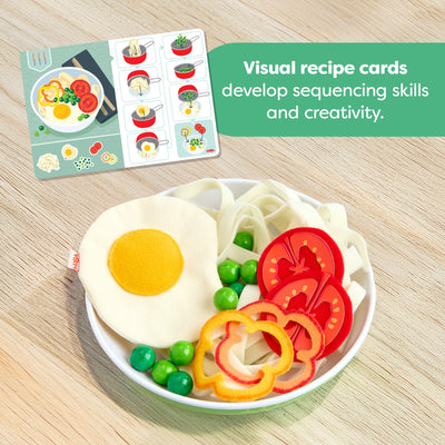 Plate of play food with vegetables and a visual recipe card from the HABA Creative Play Fresh Box on a wooden surface with text reading "Visual recipe cards develop sequencing skills and creativity'