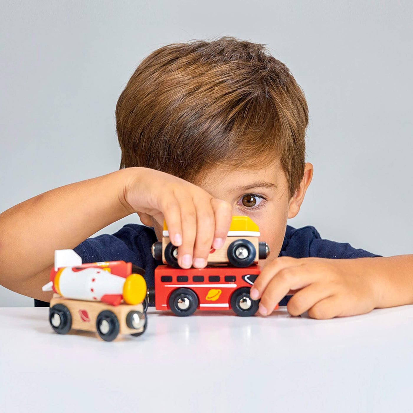 Child playing with toy wooden train cars on a white surface
