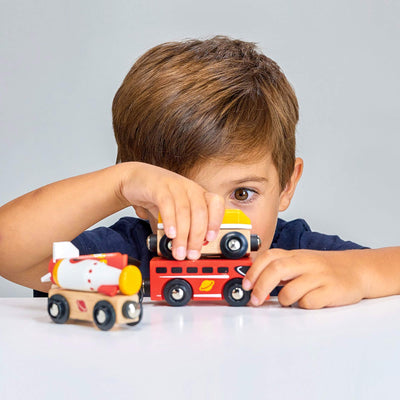 Child playing with toy wooden train cars on a white surface