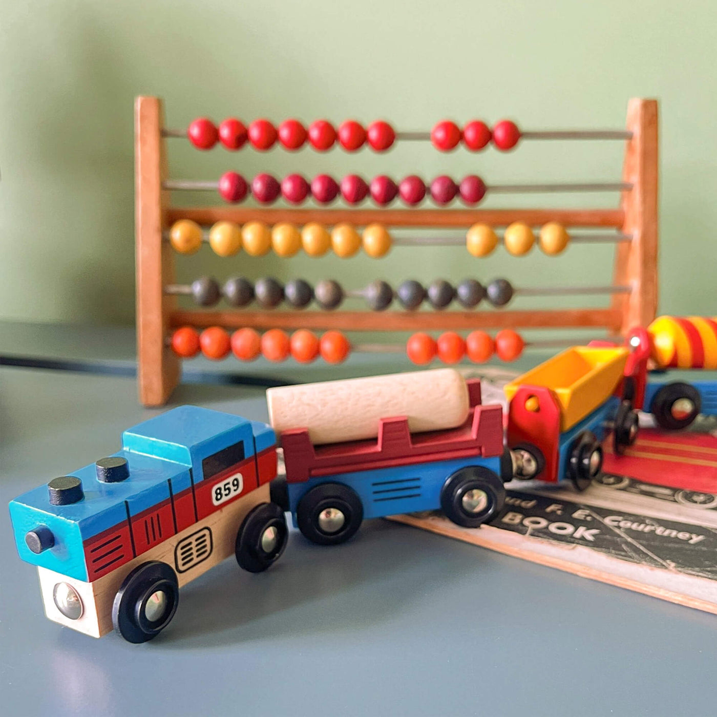 Wooden toy train set with colorful cars in front of an abacus on a light surface.