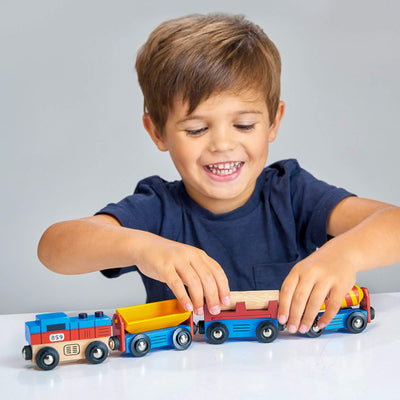 Child playing with a set of colorful toy trains on a light surface.
