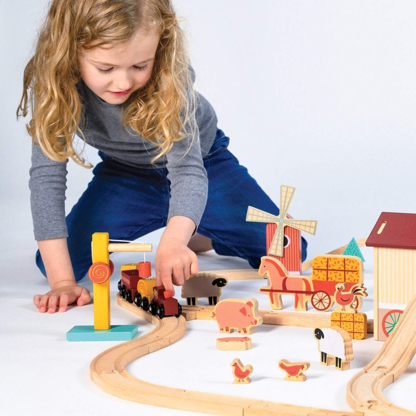 Child playing with a wooden toy train set on a white background