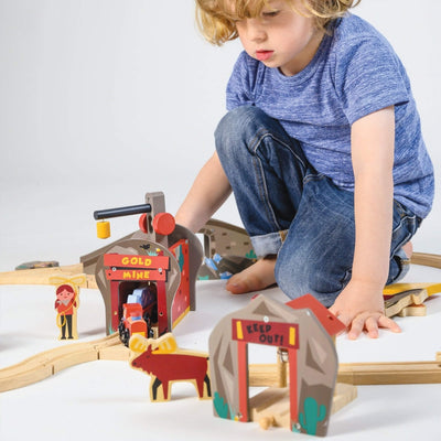 Child playing with a wooden train set on a white surface