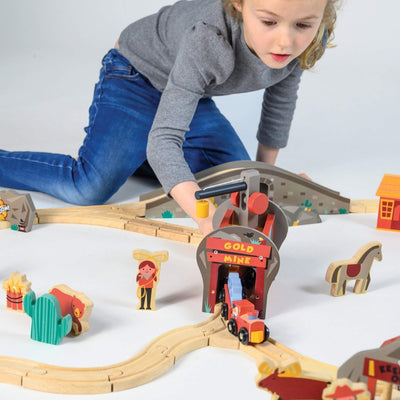 Child playing with a toy train set on a white surface