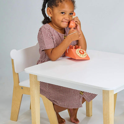 Child playing with a toy phone at a small table and chair set.