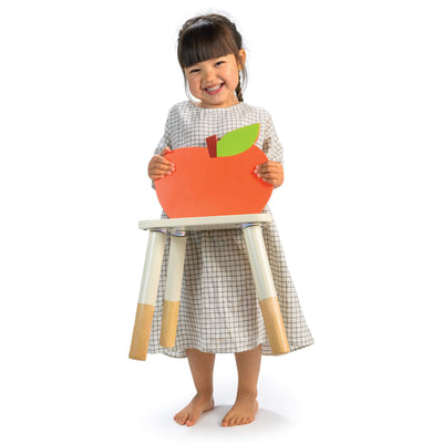 Child holding a chair with an apple shaped back rest with a smile on a white background
