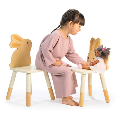 Child playing with a doll on a chair with a rabbit design.