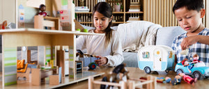 Two children at a coffee table playing with Little Friends figures, dollhouse, camper, animals, and vehicle