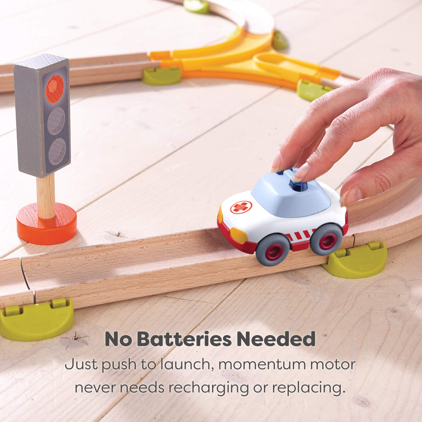 Toy car on a wooden track with a hand pushing it, accompanied by a traffic light and text explaining that no batteries are needed.