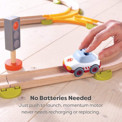 Toy car on a wooden track with a hand pushing it, accompanied by a traffic light and text explaining that no batteries are needed.