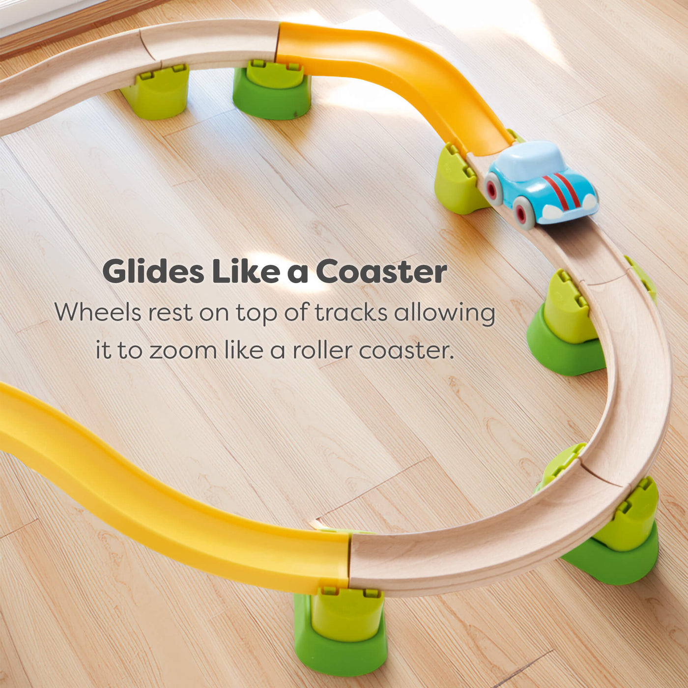 Toy track set with a car on a wooden floor, featuring text about how the car sits on top of the tracks so it glides like a roller coaster