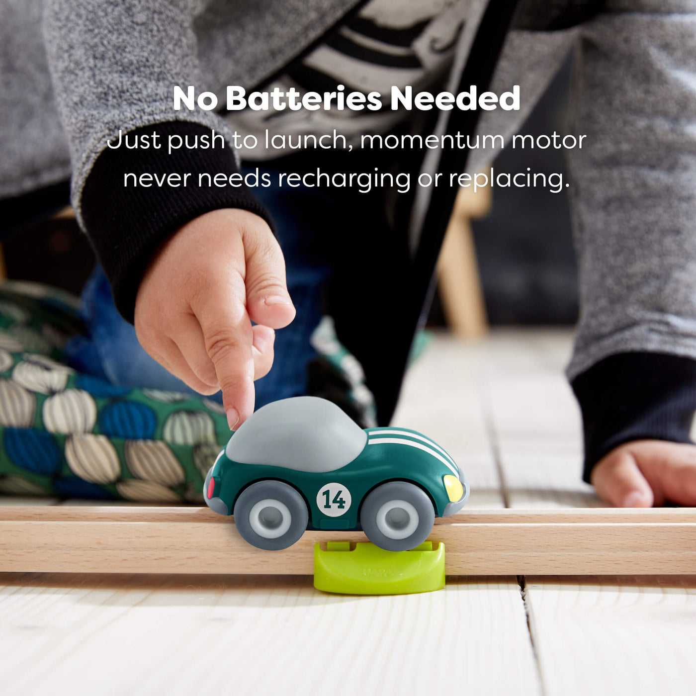 Child playing with a toy HABA car on a wooden track, with text reading "No batteries needed, just push to launch, momentum motor never need recharging or replacing."