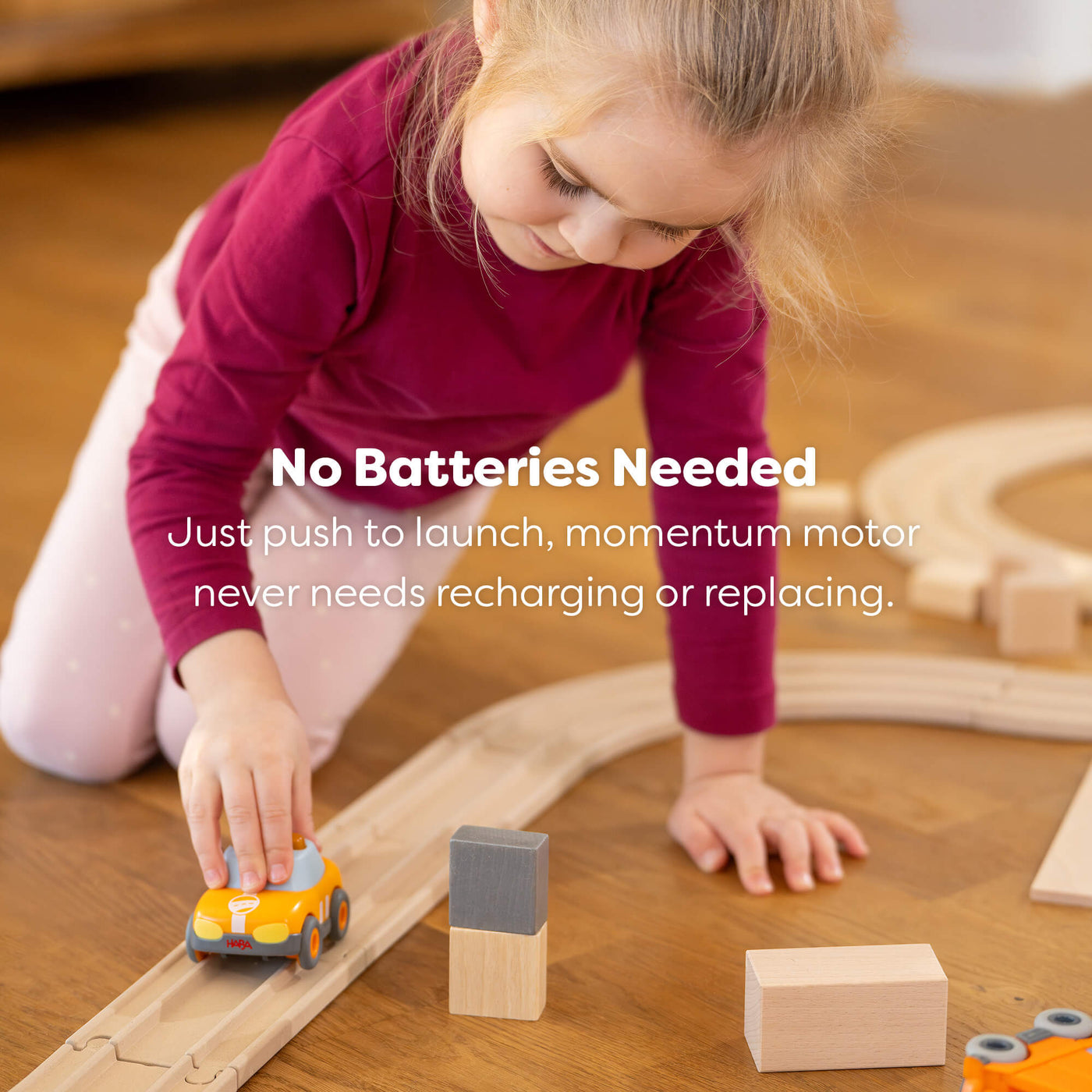 Child playing with a toy HABA car on a wooden track, with text reading "No batteries needed, just push to launch, momentum motor never need recharging or replacing."