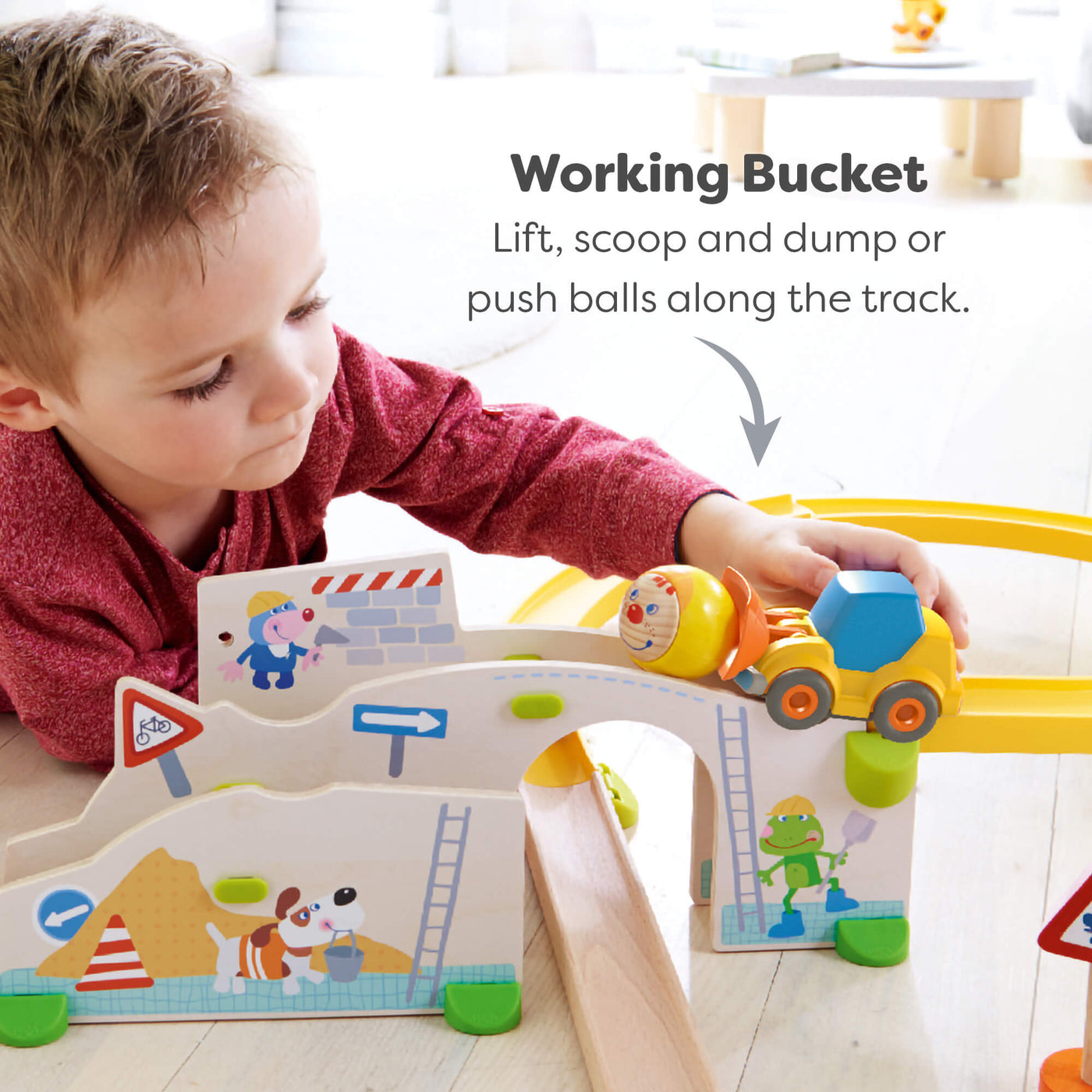 Child playing with a toy construction set with a wheel loader with working bucket on a light wooden floor.