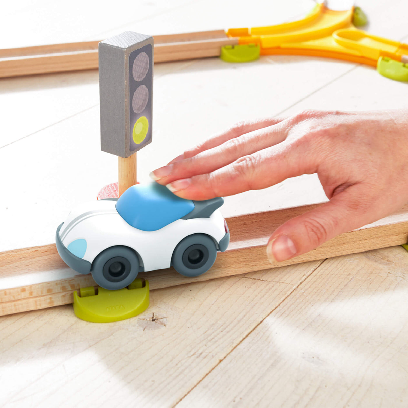 Toy car on a wooden track with a hand pushing it, featuring a green stoplight.