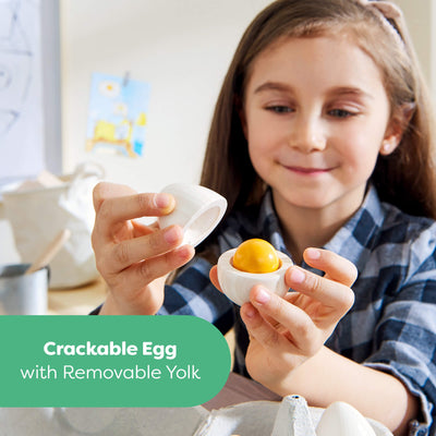 Child holding a Creative Play – Wooden Eggs Play Food Set toy egg with a removable yellow yolk, with a green label at the bottom reading 'Crackable egg with removable yolk'