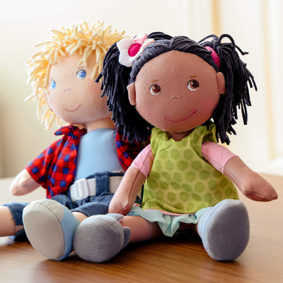 Two fabric dolls sitting on a wooden surface; one has blonde hair and the other has black hair.