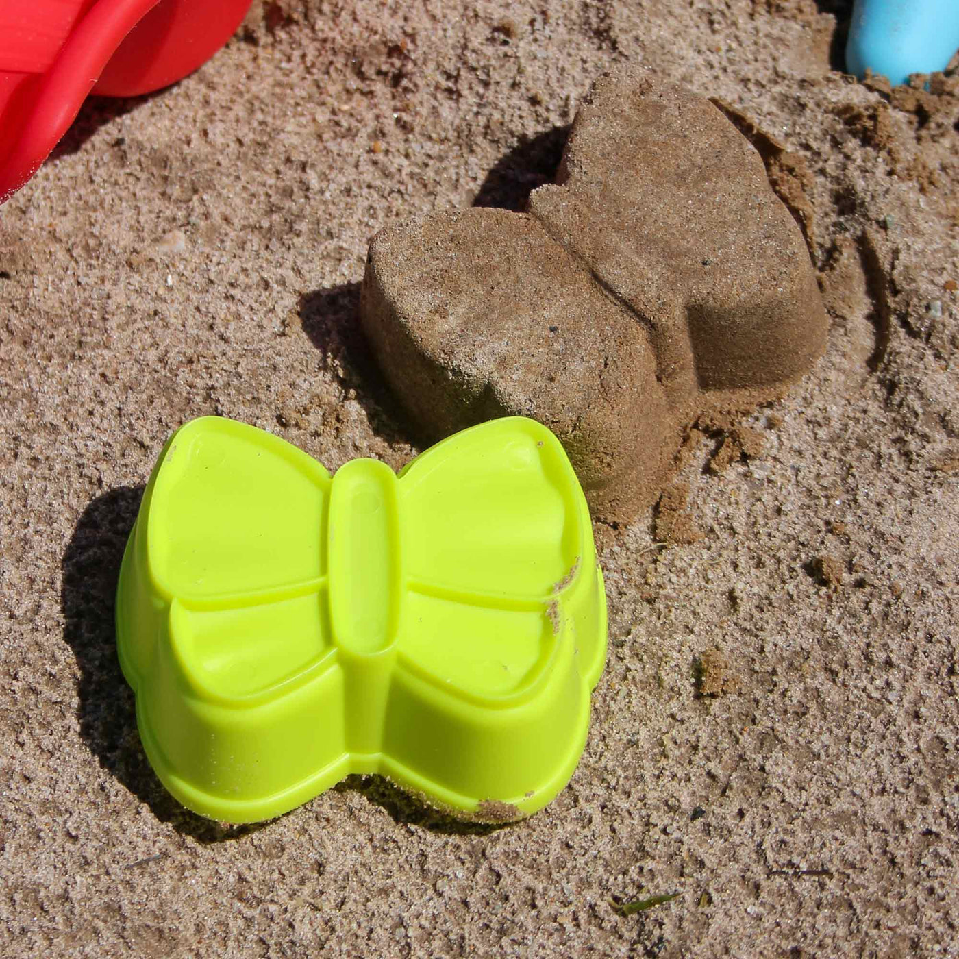 A bright yellow plastic butterfly mold lies in sand next to a sand-cast butterfly, showcasing a playful beach scene.