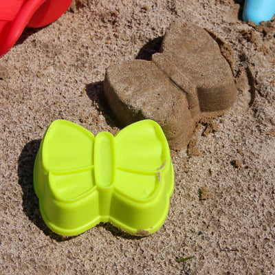 A bright yellow plastic butterfly mold lies in sand next to a sand-cast butterfly, showcasing a playful beach scene.
