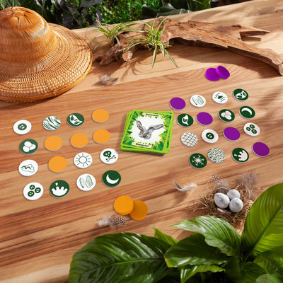 Animals Around the World Bingo components on a wooden surface with plants and a hat.